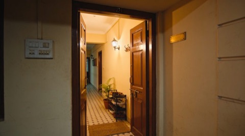 Indian apartment entrance at dusk, main door closing, a subtle status light near the frame