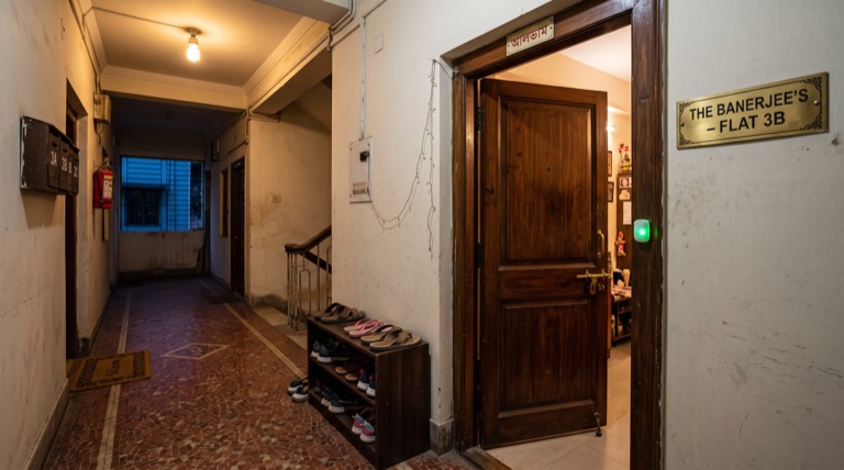 Indian apartment entrance at dusk, main door closing, a subtle status light near the frame