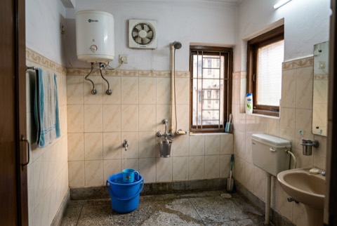 Indian bathroom in late afternoon light with wall geyser and exhaust fan